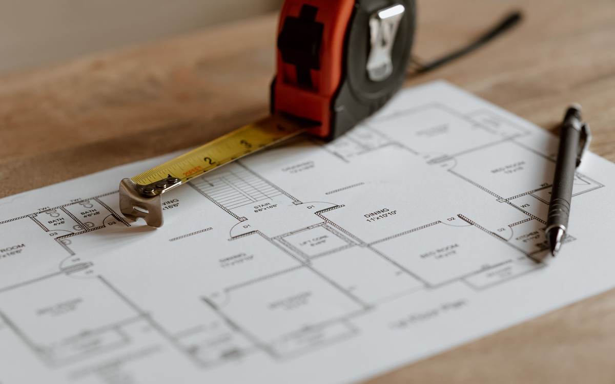 A floor plan on a table with a tape measure and a pen