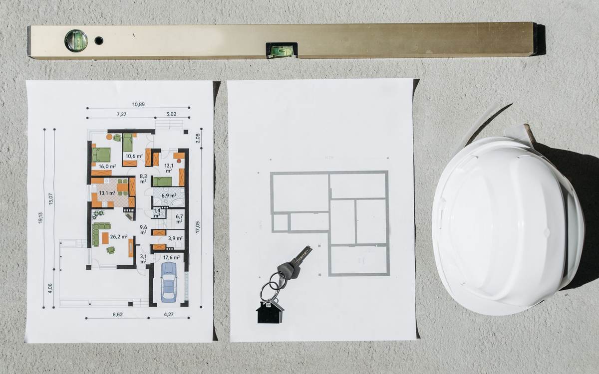 House plans, a spirit level and a hard hat laid out on concrete